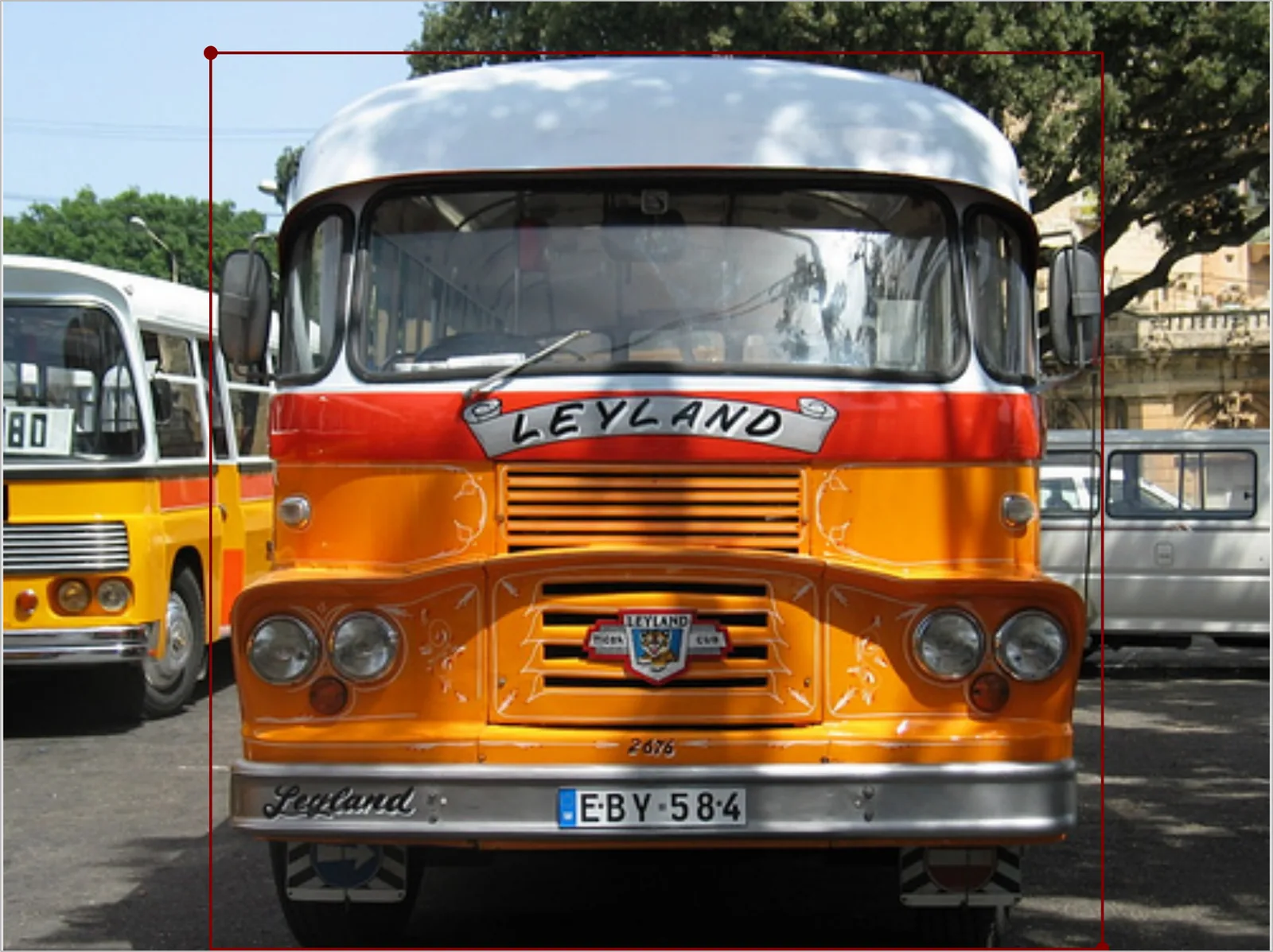 Offscreen Labelme canvas showing an orange bus annotated with a single axis-aligned rectangle whose left edge covers part of the neighboring bus and whose right edge covers a tree and a parked van.